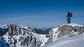 Mann Felsen am Teufelstaettkopf im Winter auf Skitour und schaut über das verschneite Berge der Ammergauer Alpen in Bayern im Winter