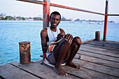 Junger Mann sitzt auf einem Dock und schreibt im Tagebuch, Barbados