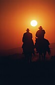 Silhouette von zwei Cowboys, die ihre Pferde bei Sonnenuntergang reiten, Texas, USA