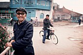 Mann lehnt an einem Geländer mit einem anderen Mann, der im Hintergrund Fahrrad fährt, China