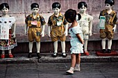 Mädchen beim Durchsuchen der zum Verkauf stehenden Kleidung auf den lebensgroßen Schaufensterpuppen von Kindern auf der Straße, China