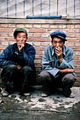 Zwei Männer rauchen Zigaretten, während sie auf dem Bürgersteig hocken, China