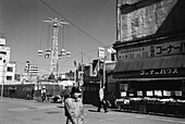 Japan, Tokyo, Man walking in street in front of Tsukiji fish market, amusement park ride in background