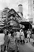 China, Hong Kong, Crowd of people walking down rundown street in old part of city, new skyscraper in background