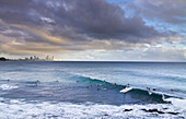 Surfers in the water on the coast of Burleigh Heads and Surfers Paradise in the background on cloudy afternoon