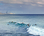 Surfer im Wasser an der Küste von Burleigh Heads und Surfers Paradise im Hintergrund am bewölkten Nachmittag