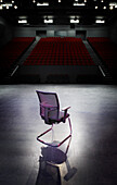 Back view of empty chair lit up on stage looking out towards empty auditorium