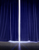 White light glowing though gap in blue stage curtains.