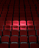 Spot light shining on a few red seats in rows of seats in auditorium