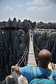 Guide beobachtet wie Frau Seilbrücke überquert, Karstlandschaft im Nationalpark Tsingy de Bemaraha, Madagaskar, Provinz Mahajanga, Afrika, UNESCO Weltnaturerbe