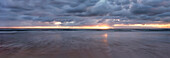 Panorama of sun setting on the horizon where the sea meets the stormy sky