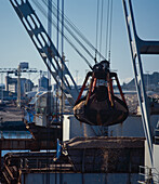 Nahaufnahme eines großen Klaueneimers, der Holzspäne auf das Schiff im Hafen lädt
