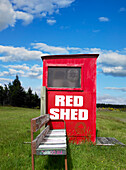 Alte öffentliche Telefonzelle rot gestrichen und alter Sitz mitten im grünen Feld