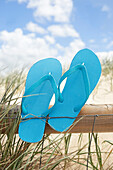 Flip Flops eingeklemmt zwischen Draht und Holzgeländer am Strand