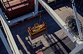 Looking down from crane at shipping container being hoisted for loading on the wharf