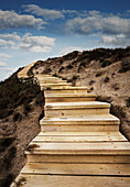 Wooden steps leading up side of sandy hill to blue sky and clouds in sky