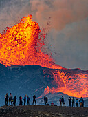 Wanderer erfreuen sich am Feuerwerk vom Observation Hill, während glühende Lava aus dem Vulkan Fagradalsfjall in Island ausgestoßen wird
