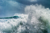 Riesige Welle, die sich während des Zyklons Ola mit stürmischem Himmel kräuselt und bricht