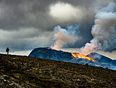 Einsamer Wanderer erklimmt den Observation Hill in Richtung glühender Lava und Dampfwolke vom Vulkan Fagradalsfjall, Island