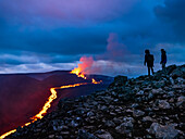 Wanderer sehen einen glühenden Fluss aus Magma und Lavakaskaden, Vulkanausbruch des Fagradalsfjall bei Geldingadalir, Island