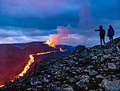 Hikers view glowing river of magma and lava cascades, Fagradalsfjall Volcanic eruption at Geldingadalir, Iceland