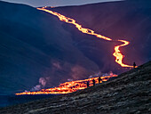Wanderer betrachten den glühenden Magmastrom des Vulkanausbruchs Fagradalsfjall bei Geldingadalir, Island