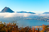 Berggipfel San Salvatore über Wolkengebilde und Luganersee mit Sonnenlicht und klarem Himmel in der Stadt Lugano, Tessin in der Schweiz