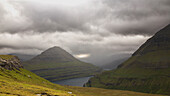 Funning Fjord, Eysturoy, Faeroere framed by green mountains. Dark clouds, cloud gap, sunshine