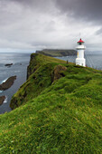Blick auf Steilküste und  Mykines Holmur Leuchtturm bis Mykines, Färöer Inseln. Dunkle Wolken.
