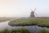 Bucket mill in the fog, Neustadt-Gödens, Friesland, Germany. Windmill on a meadow with a moat.