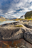 Gimsoy Kirke. Foreground rocky coast. background mountains. Gimsoy, Nordland, Lofoten, Norway.