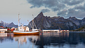 Hamnoy harbor in front of a mountain backdrop with a fishing boat. Reine, Lofoten, Nordland, Norway.