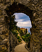 View through a stone arch in the Jardin Exotique of Èze on old houses of the village, Èze, French Riviera, France