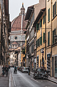 Bicycle riders in alley with Duomo, Cathedral of Santa Maria del Fiore in background, Florence, Tuscany, Italy