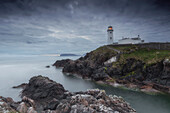 Fanad Head lighthouse on rocky coast. calm sea. cloudy. Arryheernabin, County Donegal, Ireland.