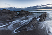 Surf laps rocks on Black Beach. Little Island Bay Beach, County Cork, Ireland.