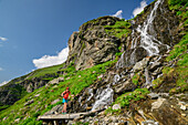 Mountaineering woman walking on bridge over waterfall, Floitental, Zillertal Alps Nature Park, Zillertal Alps, Tyrol, Austria
