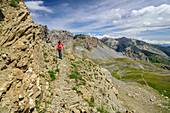 Frau beim Wandern steigt über Felsband ab, Col Sautron, Chambeyron-Gruppe, Val Maira, Cottische Alpen, Piemont, Italien