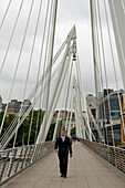 Businessman walking over Jubilee Footbridge next to Cannon St Railway Bridge, London, UK