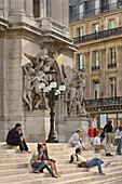 Menschen sitzen auf den Stufen der Pariser Oper, Frankreich, Ile-de-France, Paris. Place de l'Opera