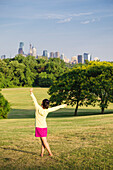 Girl dancing in park in front of city skyline, Philadelphia, USA
