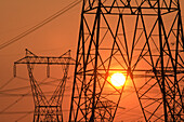 Electricity pylon and power lines with sun behind.