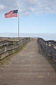 Boardwalk durch Grasland mit Bergen und amerikanischer Flagge, USA