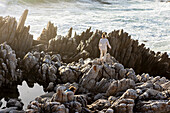 Two children exploring the jagged rocks and rock pools on the Atlantic Ocean coastline, De Kelders, Western Cape, South Africa.