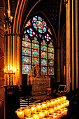 Innenraum der Kathedrale Notre Dame in Paris, vor dem Brand von 2019, ein Buntglasfenster und Reihen brennender Kerzen