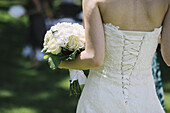 Eine Braut in einem eng anliegenden Oberteil, weißes Kleid mit Schnürungen über den eng anliegenden Rückenteilen.