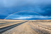 Eine Interstate Highway, die durch eine flache Landschaft bis zum Horizont reicht, ein Regenbogen über der Straße, USA