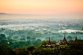 Erhöhter Blick auf die Ebene der Tempel in Mandalay, Stupas und Türme, die aus dem Nebel auftauchen, historische buddhistische Stätten, Myanmar