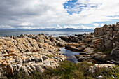 Rocky jagged coastline, rock pool and view out to the ocean, De Kelders, South Africa