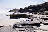 Teenager-Mädchen liegt auf dem Rücken auf Felsen über einem Sandstrand, Walker Bay Naturreservat, Südafrika